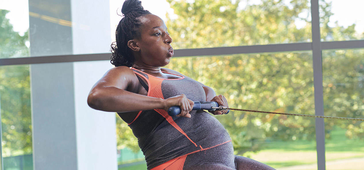 A pregnant woman works out on a rowing machine.