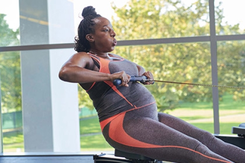 A pregnant women works out on a rowing machine.