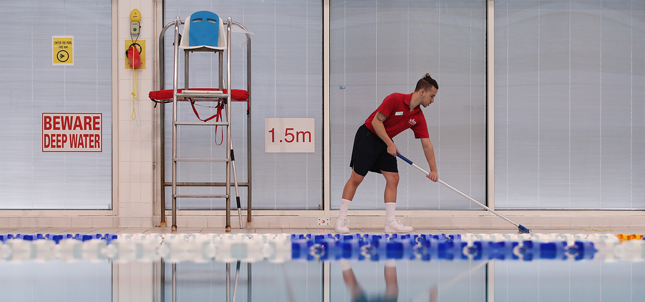 A man cleans the side of an indoor swimming pool
