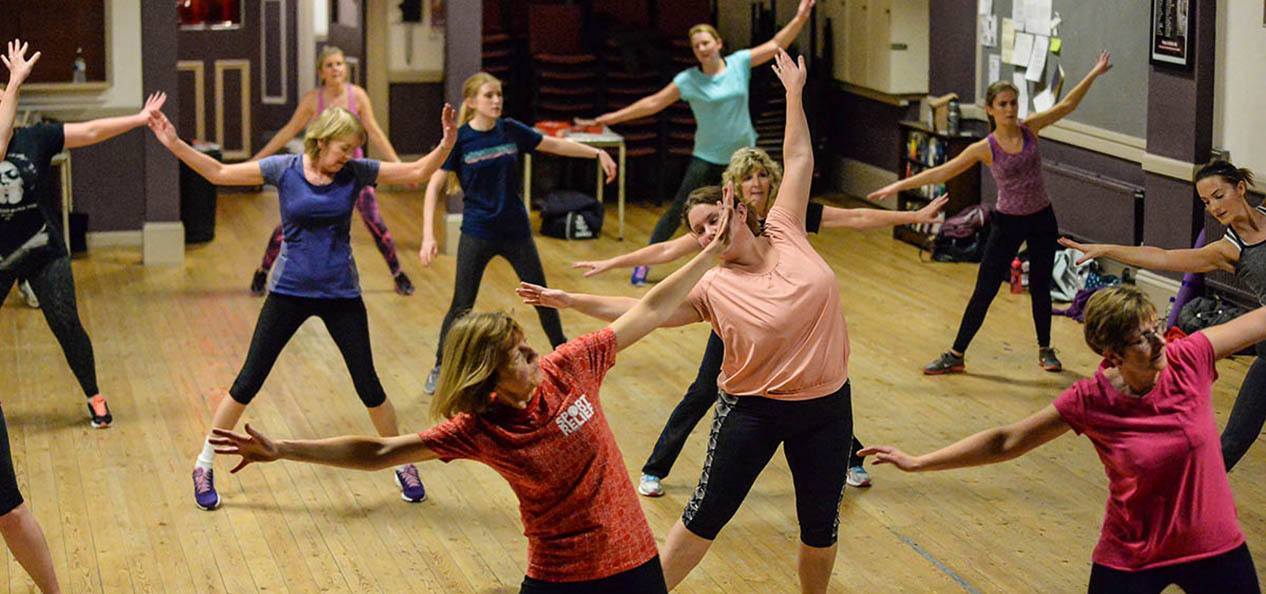 A group of women do an exercise class in a village hall