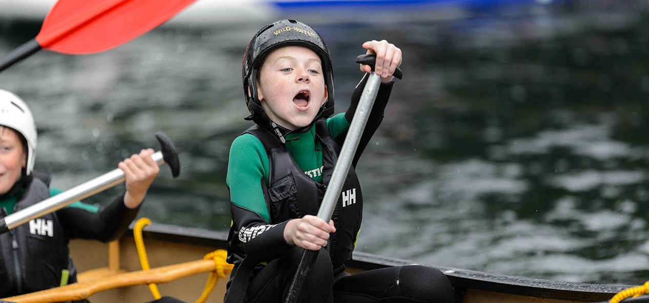 A boy cries out in joy while paddling in a canoe.