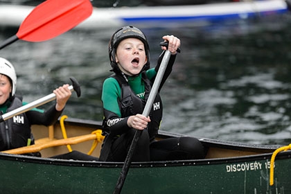 A boy cries out in joy while paddling in a canoe.