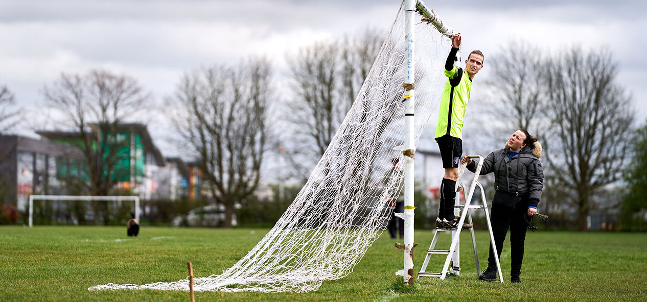 A man and a women set up the nets on a football goal before a game.