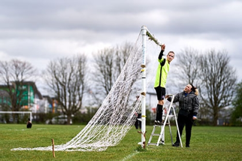 A man and a woman set up the nets on a football goal before a game.