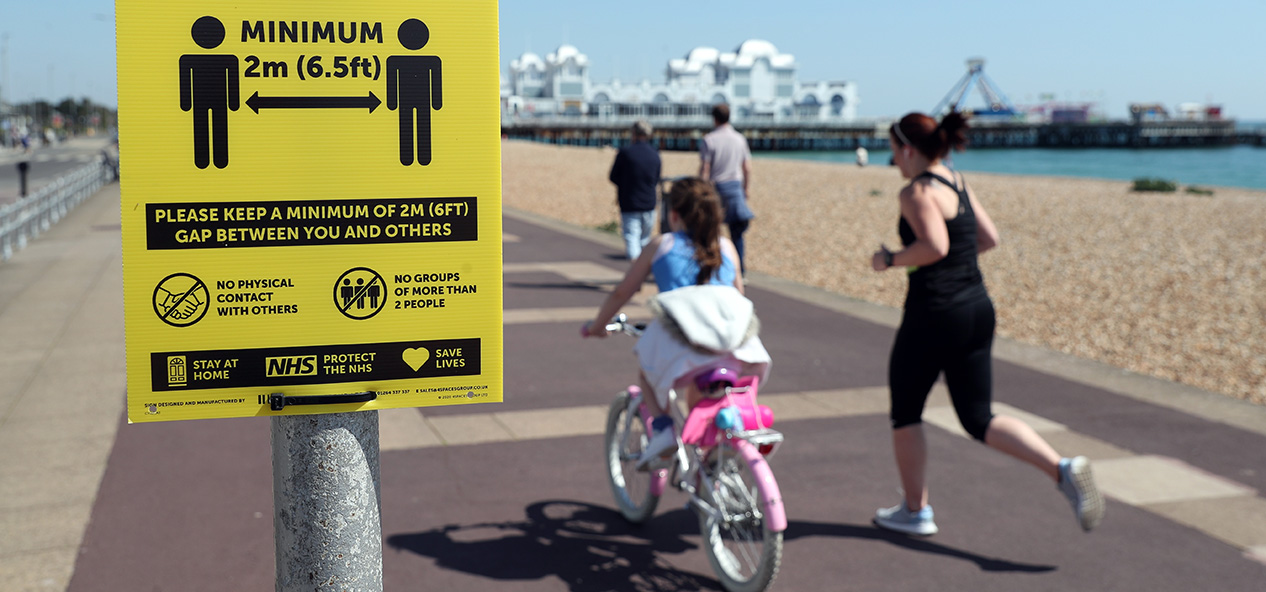 People exercise on Southsea seafront, running and riding past a sign reminding people to social distance.