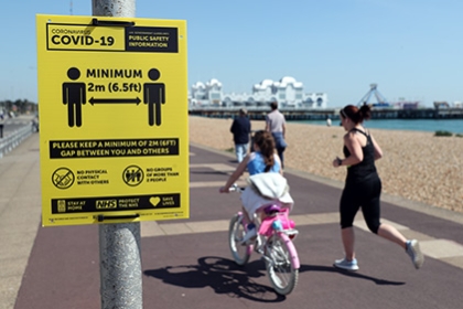 People exercise along Southsea seafront, running and riding past a sign warning about social distancing.