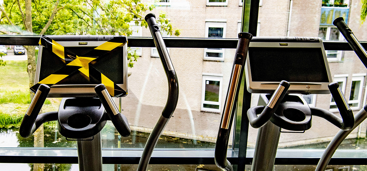 An indoor gym with tape over some machines to enable social distancing