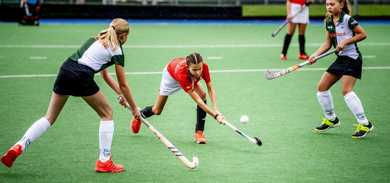 A girls' hockey match with one girl hitting the ball as opposition players close her down.