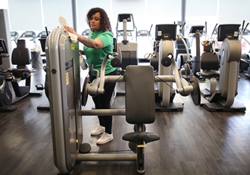 A gym worker wipes down a weights machine