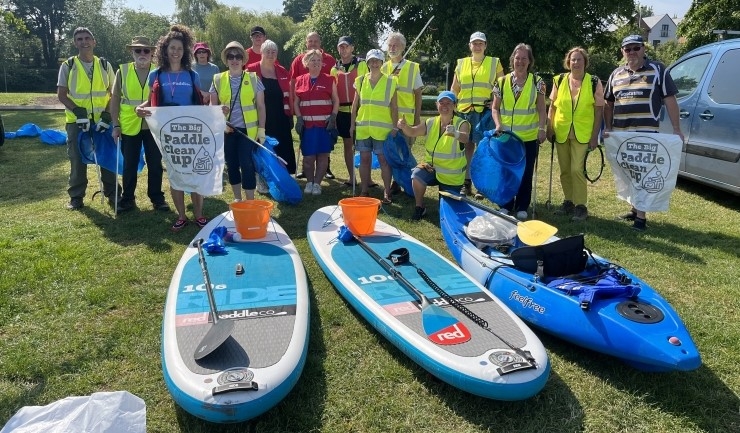 A group of people in high-vis vests pose for a photo, in front of paddle boards and a canoe, holding litter pickers and big bags