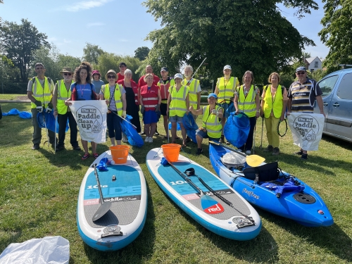 A group of people in high-vis vests pose for a photo, in front of paddle boards and a canoe, holding litter pickers and big bags