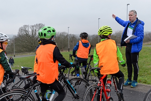 A group of young cyclists listen to their coach