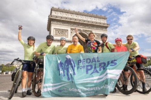 Chris Boardman, Dame Katherine Grainger and the Pedal for Paris cycle team pose with their bikes, a flag and arms raised in front of the Arc de Triomphe.