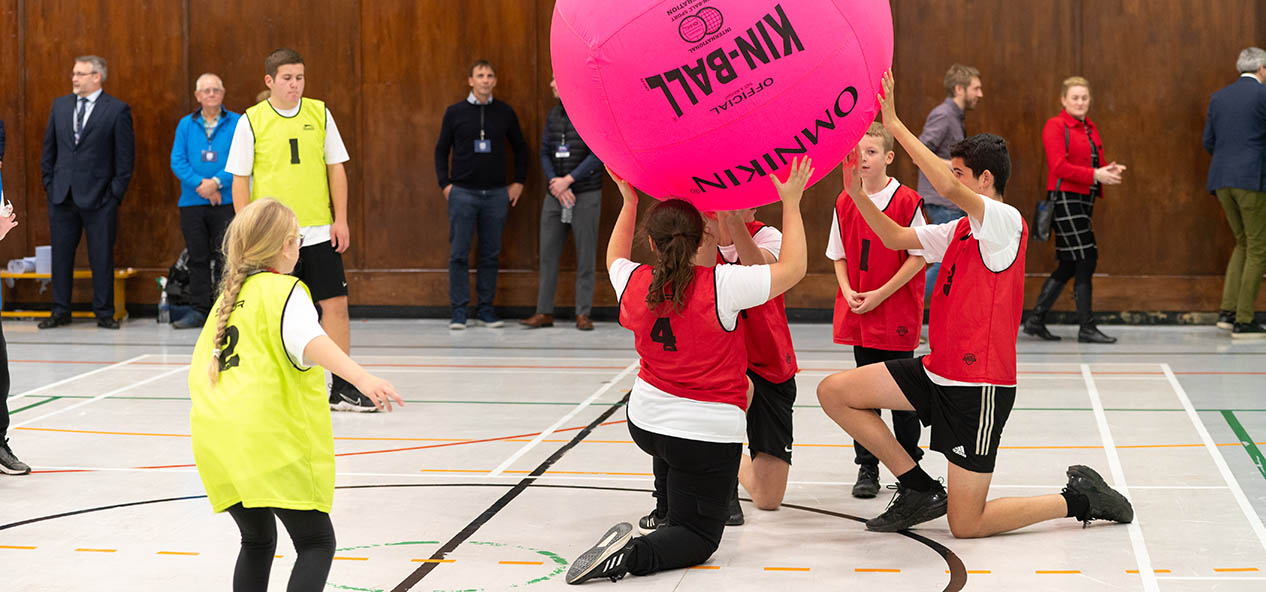 A group of people play with a giant ball on an indoors hall.