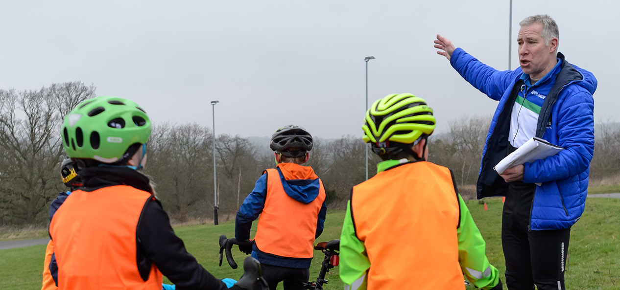 A group of young cyclists listen to their coach