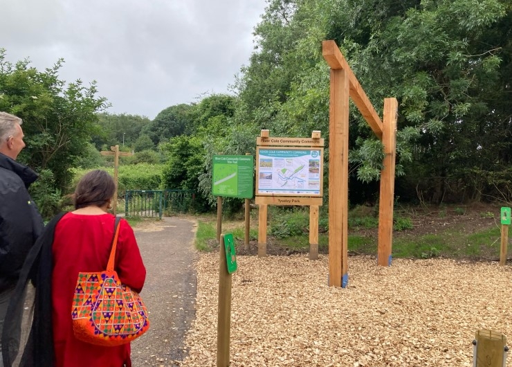 Two people walk by wooden signs to enter a park.