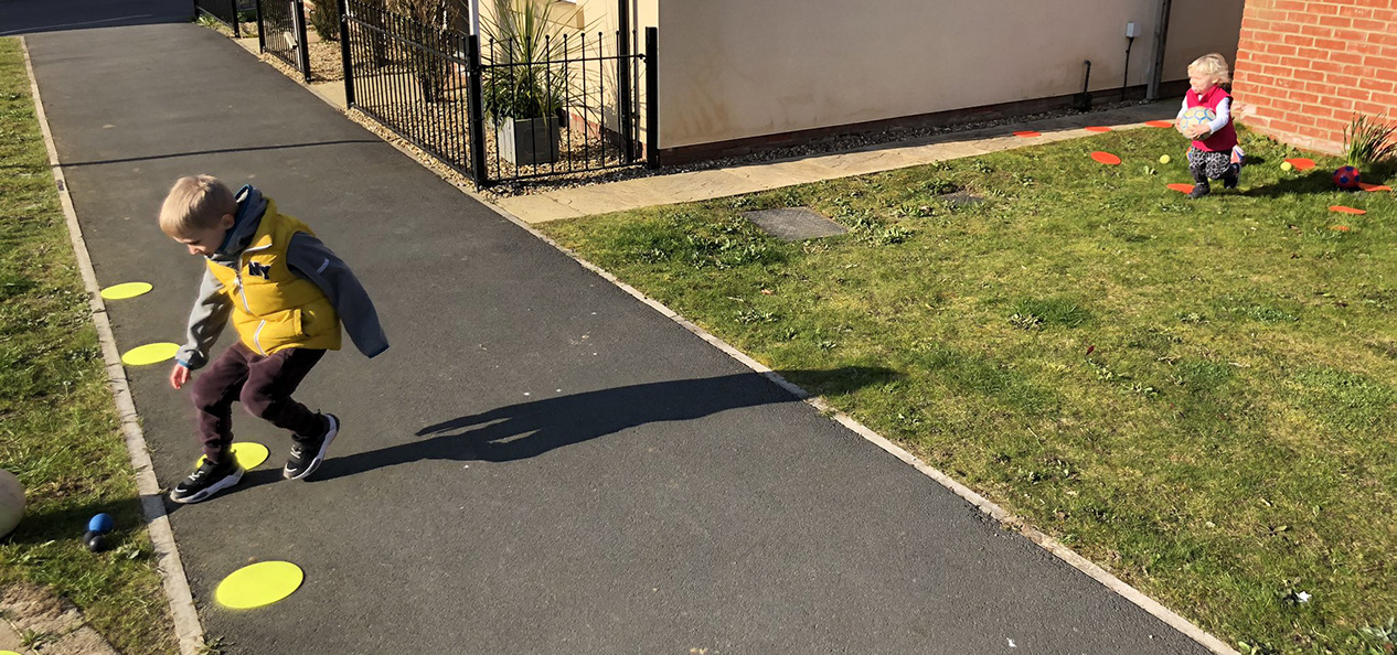 Two young children play an improvised game using cones and balls in their front garden.