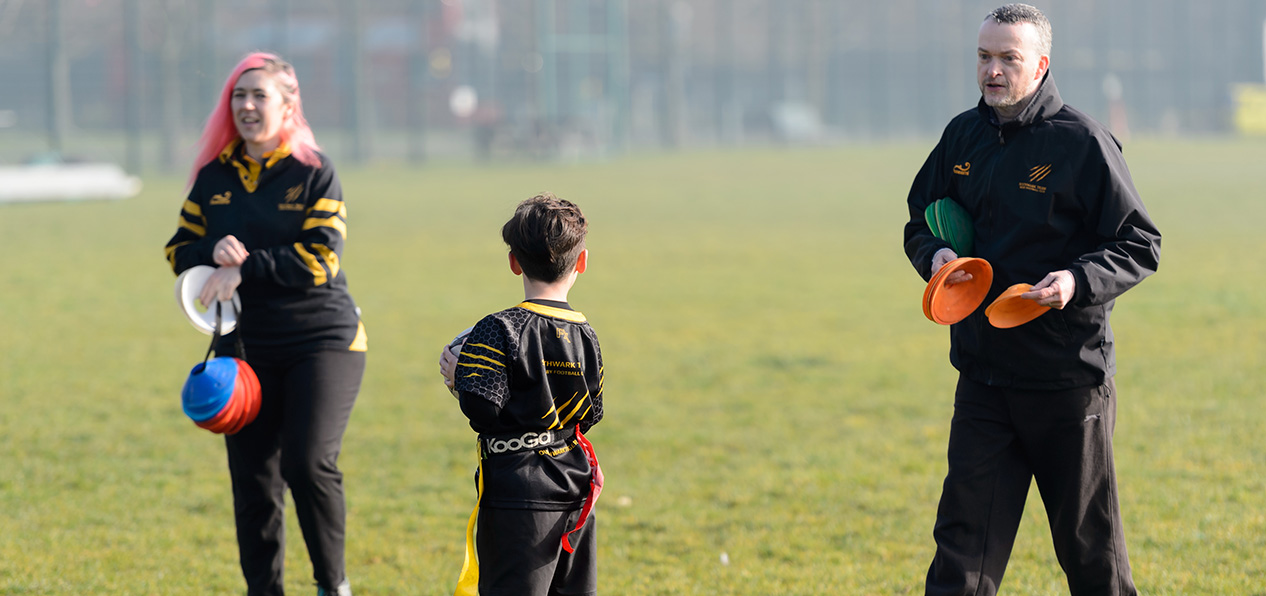 Two volunteers talking to a child on a playing field.