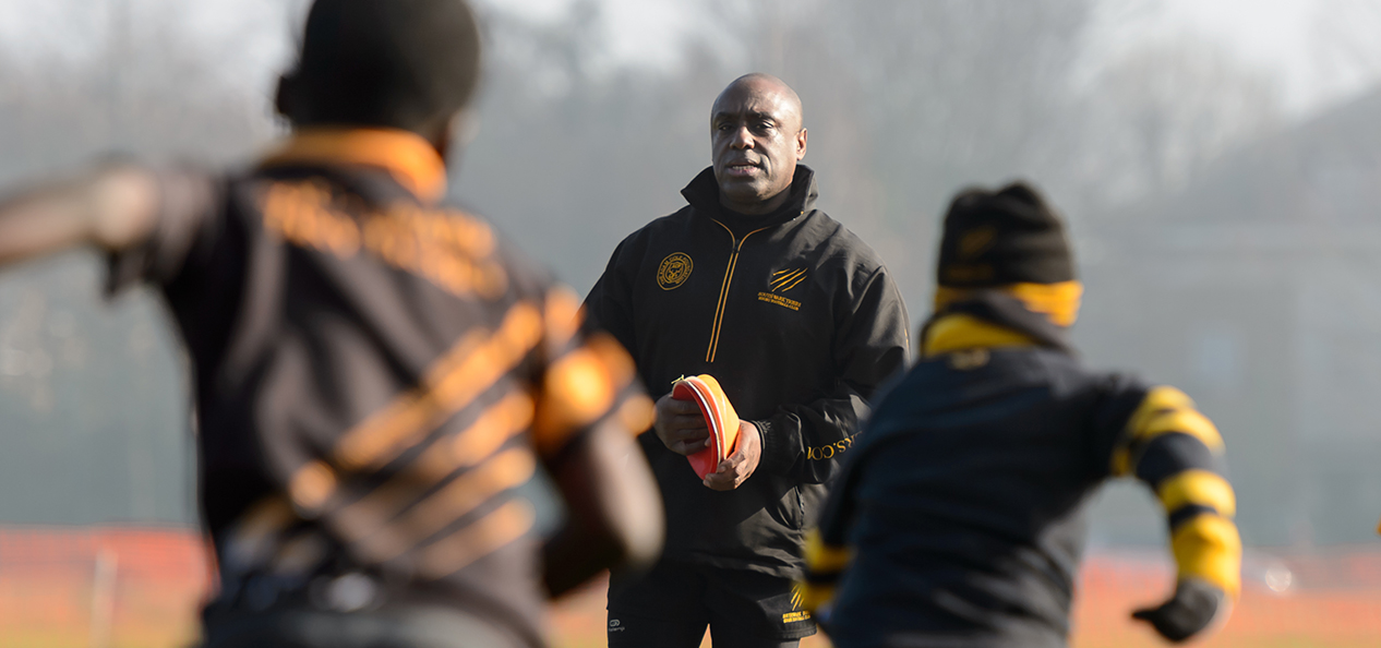 A junior rugby coach watches on as two players run towards him