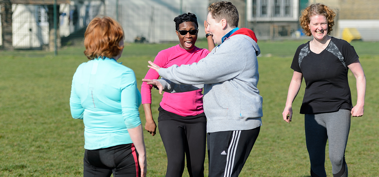 A group of people chatting and smiling on a rugby field.