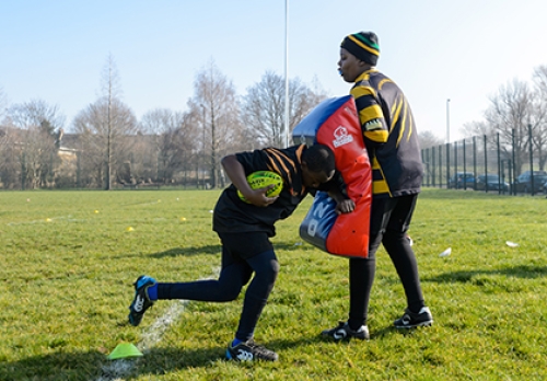 Two rugby players perform a tackling drill with one holding a tackling pad