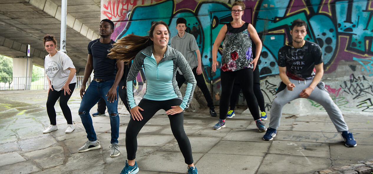 A groups of people doing exercise outside, in front of a graffiti mural