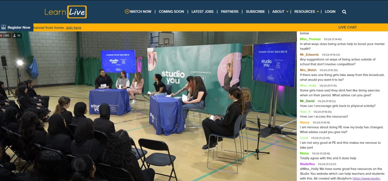 A screengrab of a website hosting a live streaming of a panel discussion in front of students in a secondary school sports hall. A stream of live questions is shown on the right.