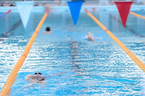 People swimming in lanes in a pool, with flags above