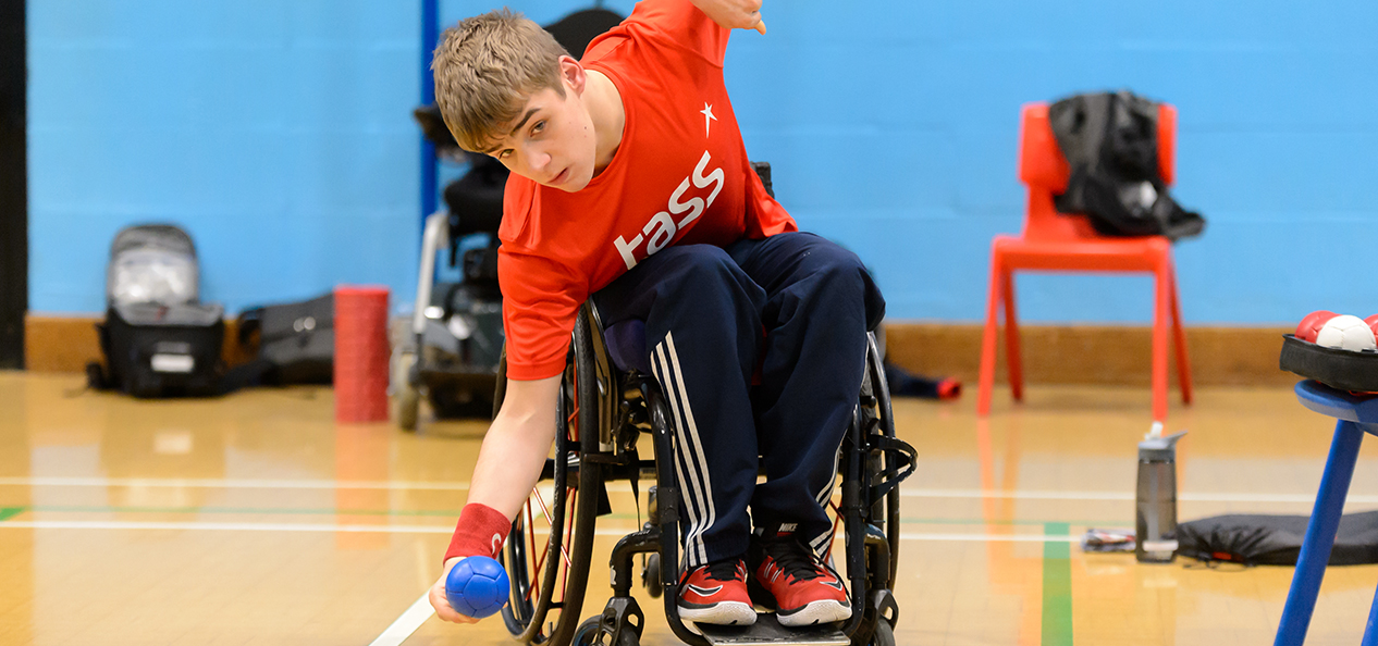 A young man in a wheelchair playing boccia in a sports hall.