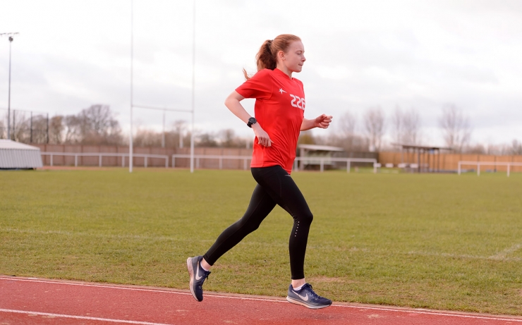 A girl wearing a red TASS t-shirt runs round an athletics track.