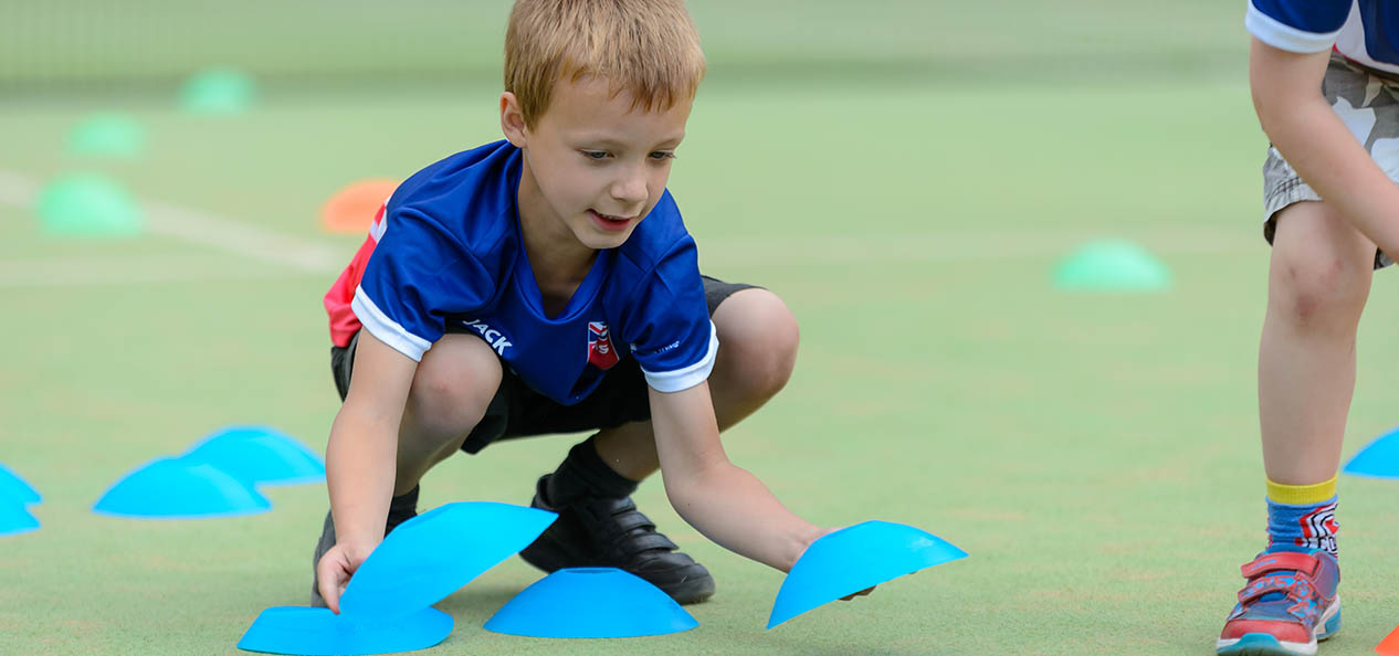 A boy laying out cones on the ground before the start of a tennis session.