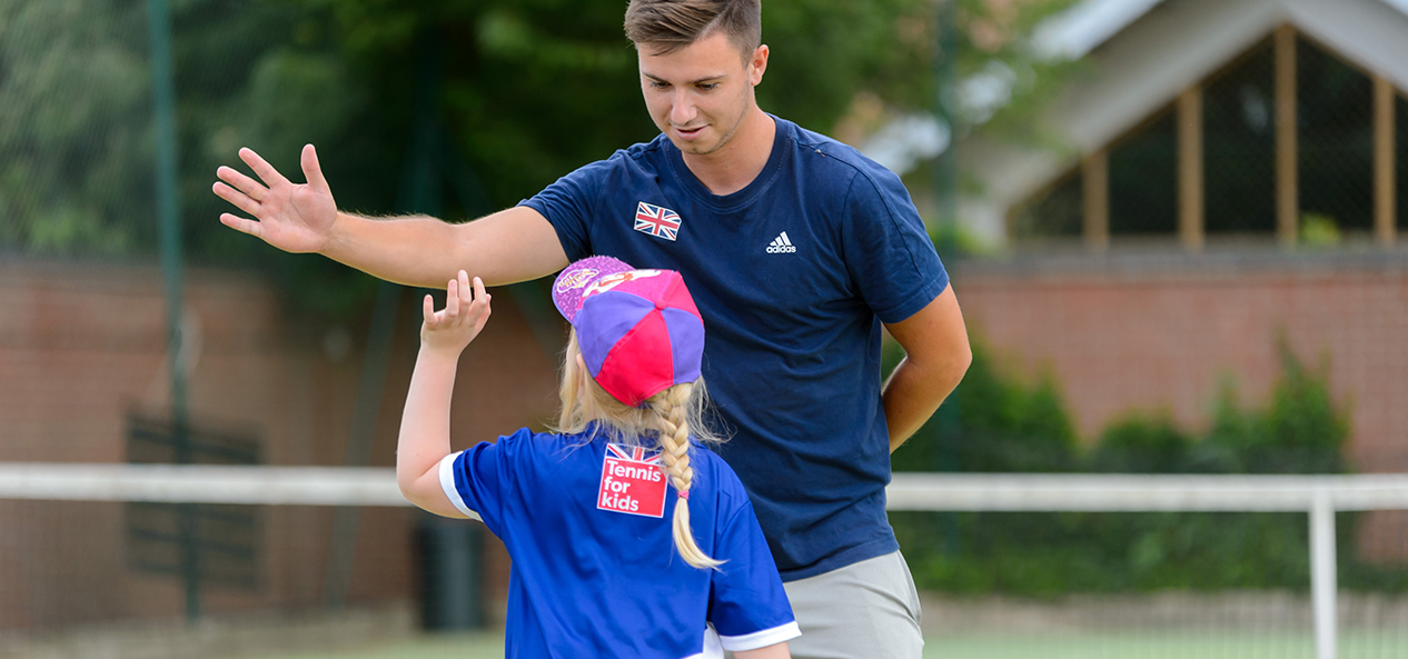 A tennis coach high fives a girl during a training session