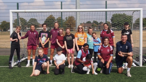 A group of girls, with a male coach, pose for a photo in a football goal