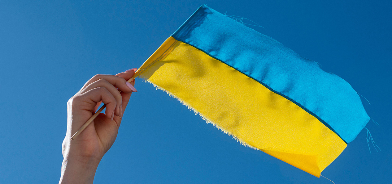 A small Ukrainian flag being waved against a blue sky