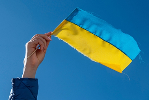 A small Ukrainian flag being waved against a blue sky