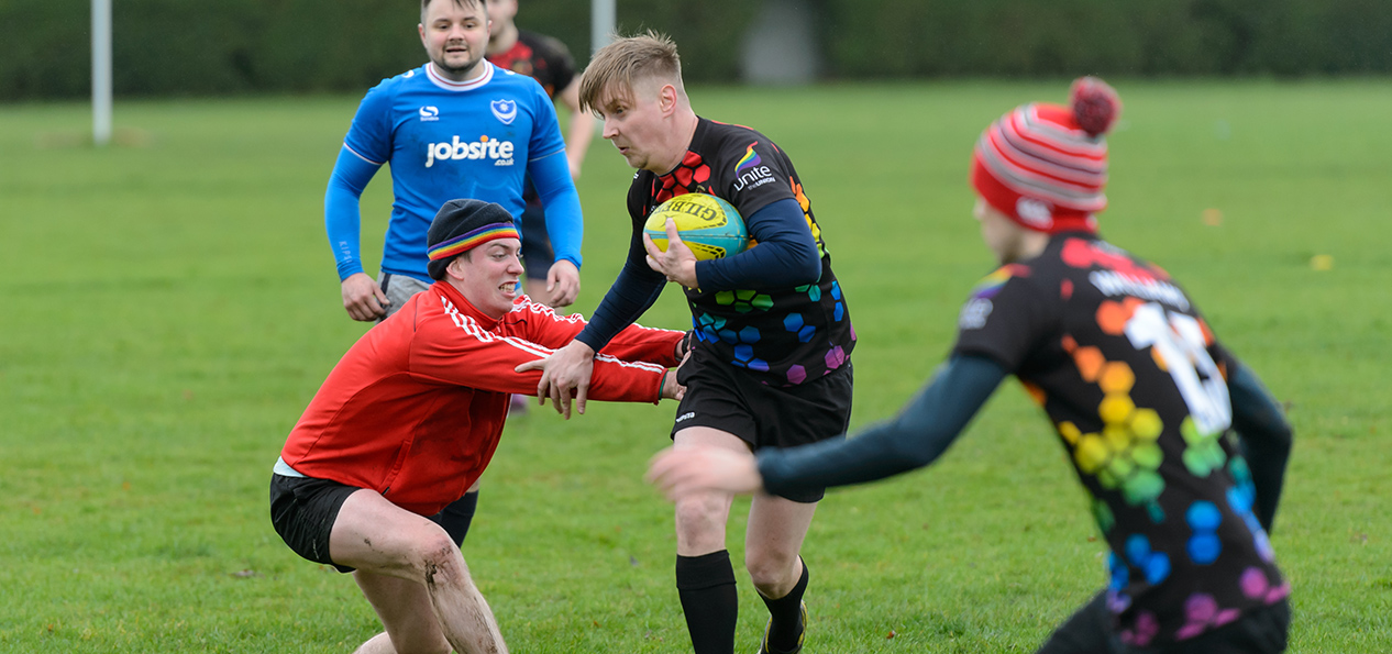 A man attempts to tackle another man, running with a rugby ball.