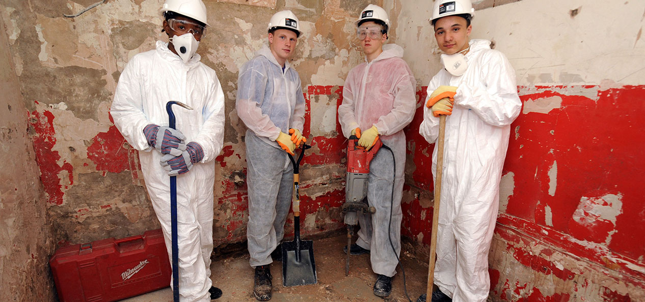 A group of Volunteer it Yourself volunteers - all teenage boys - pose for a photo in overalls during renovation works on a community sports facility.