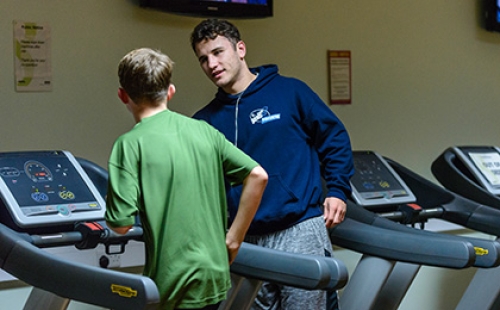 A Street Games volunteer instructs a boy how to run on a treadmill