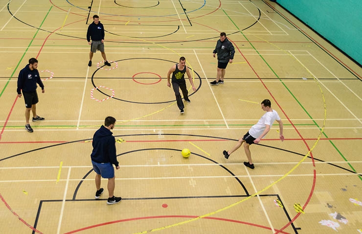 An overhead shot of a group of people playing football in a sports hall.