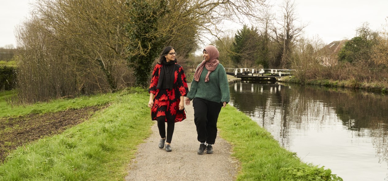 Two women walk side-by-side on a path beside a canal.