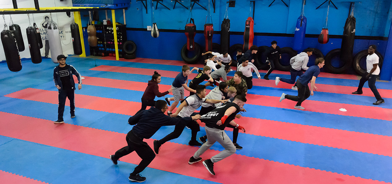 A group of young people play a game of tag in a boxing gym.