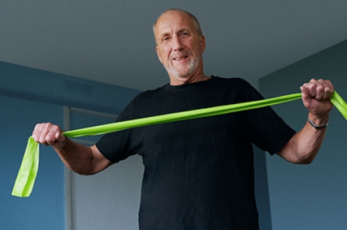 A man performs exercises at home using a resistance band.