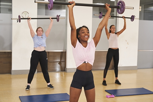 Three women lift weights above their head in a HiiT class