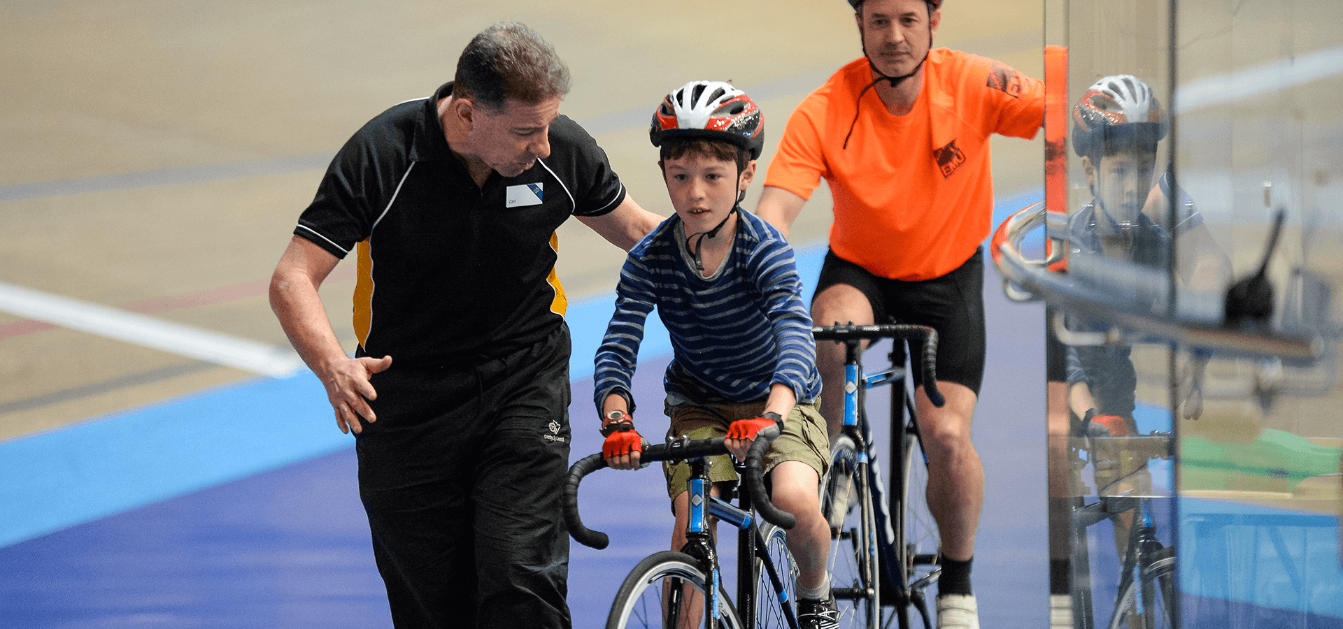 Coach helping young boy cycling on velodrome