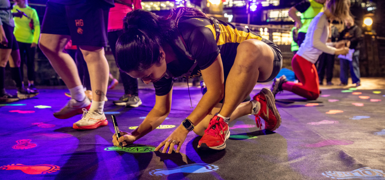 A runner writes on a glow-in-the-dark footprint sticker on the ground