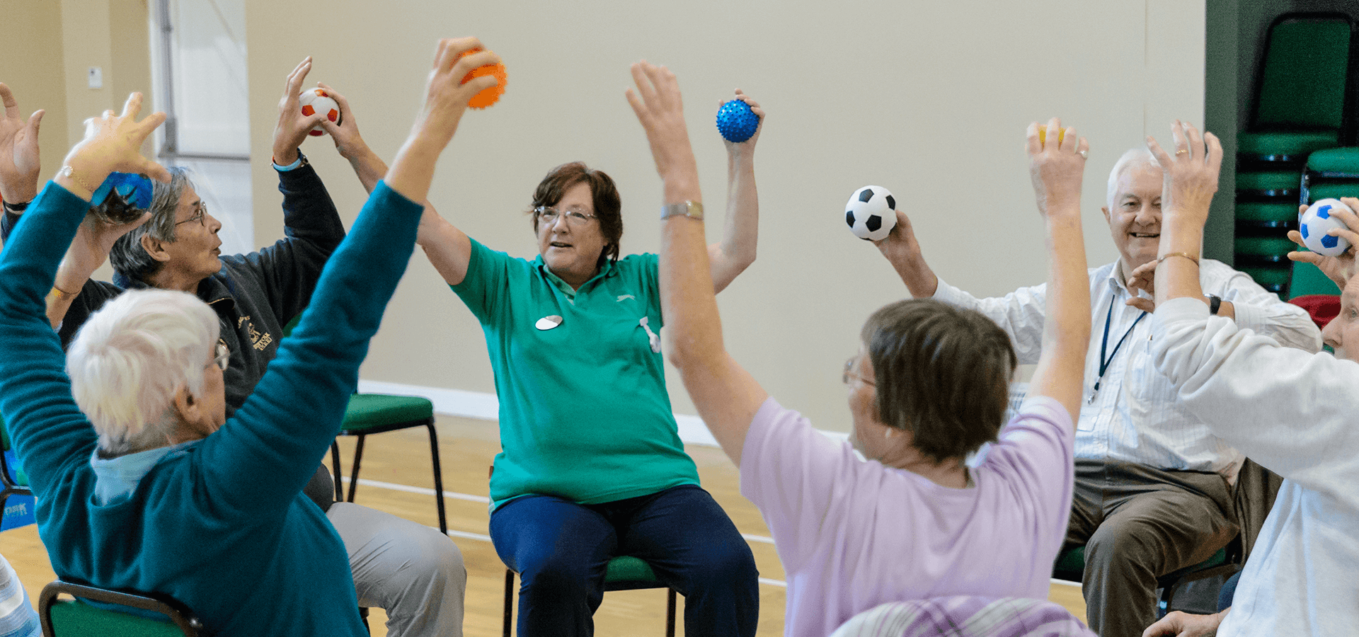 A class takes part in sitting exercises with mini footballs